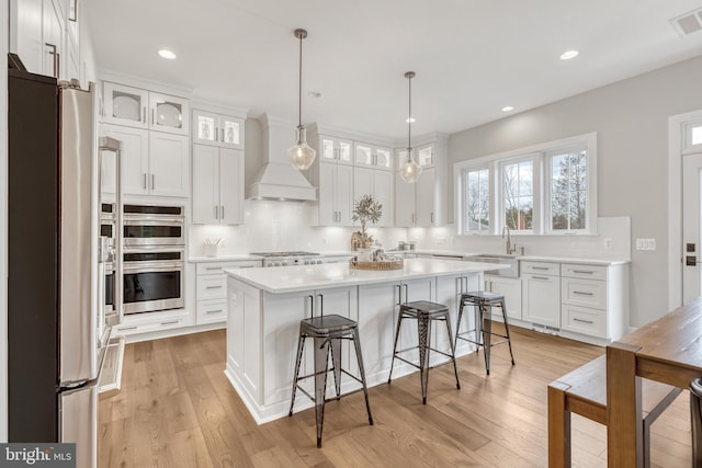 kitchen with appliances with stainless steel finishes, custom range hood, decorative backsplash, and a kitchen breakfast bar