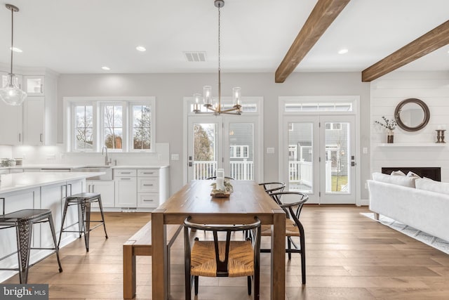 dining room with light wood-type flooring, a wealth of natural light, visible vents, and beamed ceiling