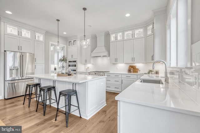 kitchen featuring a breakfast bar area, custom exhaust hood, stainless steel appliances, a sink, and a kitchen island