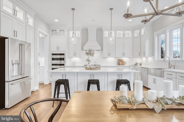 kitchen with premium range hood, a sink, white cabinets, appliances with stainless steel finishes, and a center island