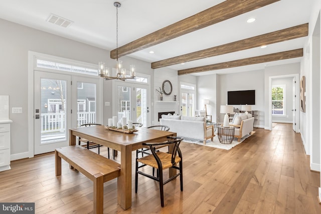 dining room featuring visible vents, baseboards, light wood-style flooring, a fireplace, and a notable chandelier