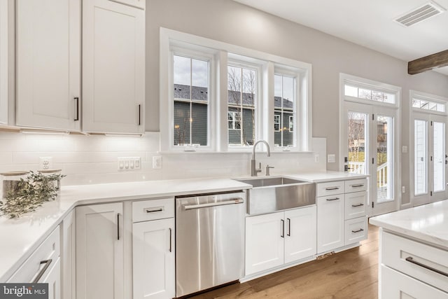 kitchen featuring light wood finished floors, visible vents, backsplash, stainless steel dishwasher, and a sink