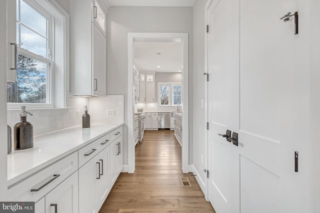 interior space with light wood-type flooring, visible vents, dishwasher, and decorative backsplash