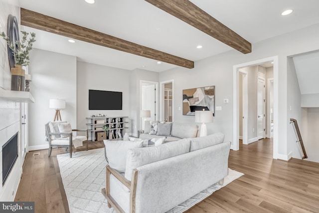 living area featuring baseboards, a glass covered fireplace, beamed ceiling, light wood-style floors, and recessed lighting