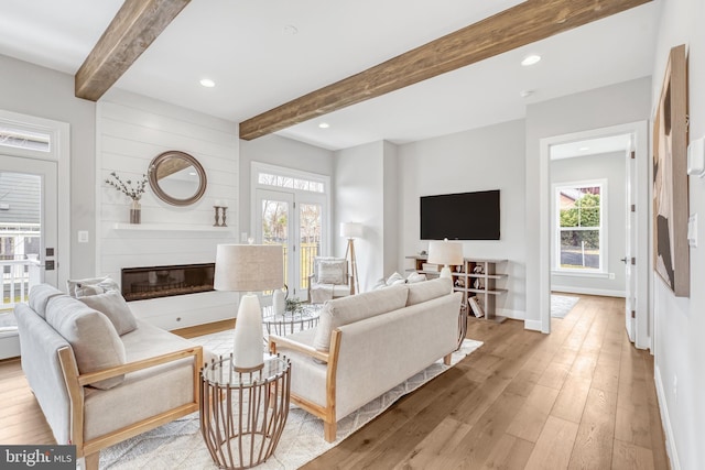 living room with light wood-style flooring, a fireplace, baseboards, and beam ceiling