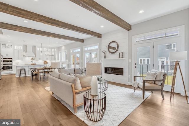 living area featuring a large fireplace, beamed ceiling, light wood-type flooring, a chandelier, and recessed lighting