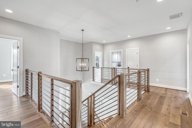 corridor featuring an inviting chandelier, wood-type flooring, visible vents, and an upstairs landing