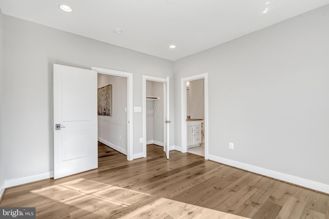 unfurnished bedroom featuring a spacious closet, wood finished floors, and baseboards