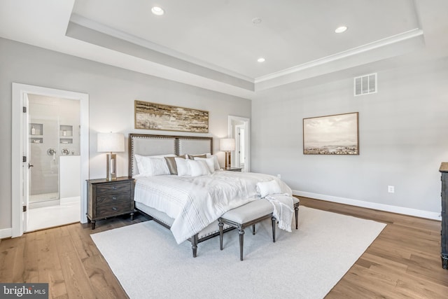 bedroom with a raised ceiling, visible vents, baseboards, and wood finished floors