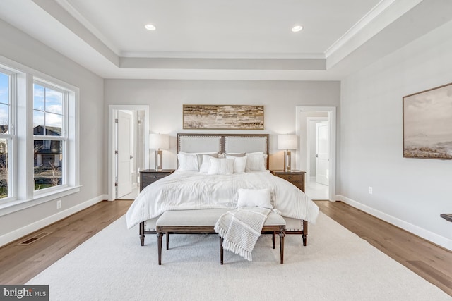 bedroom featuring a tray ceiling, baseboards, and wood finished floors