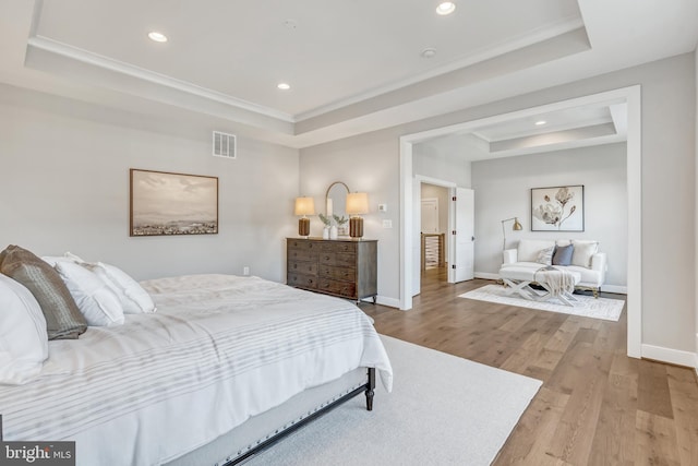 bedroom with baseboards, visible vents, a tray ceiling, and wood finished floors