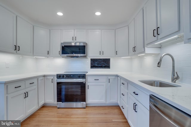 kitchen with light wood-style flooring, appliances with stainless steel finishes, white cabinets, a sink, and light stone countertops