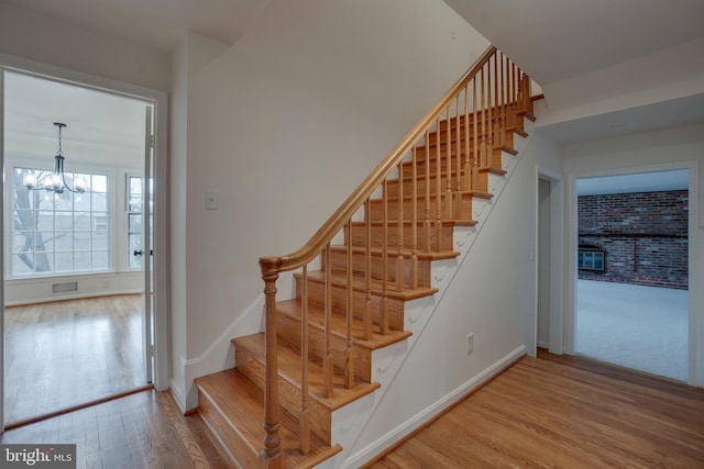 stairs featuring visible vents, a notable chandelier, baseboards, and wood finished floors