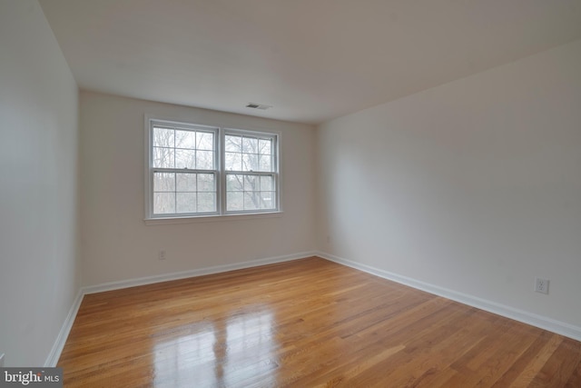 spare room featuring light wood finished floors, visible vents, and baseboards