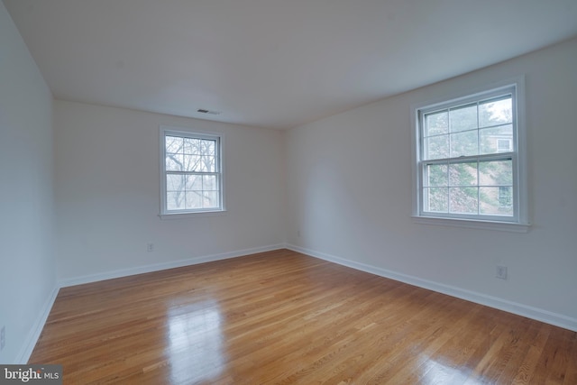 unfurnished room featuring light wood finished floors, visible vents, and baseboards