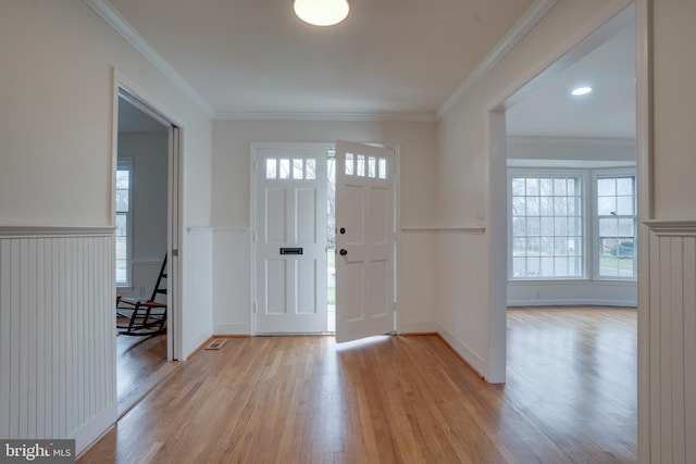 foyer with light wood-style floors, ornamental molding, and a wainscoted wall