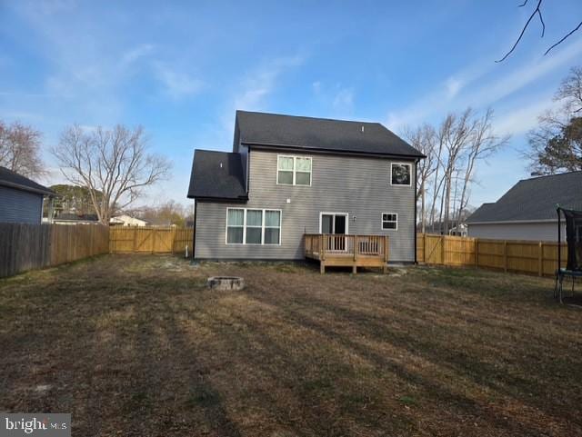 back of house with a yard, a trampoline, a wooden deck, and a fenced backyard