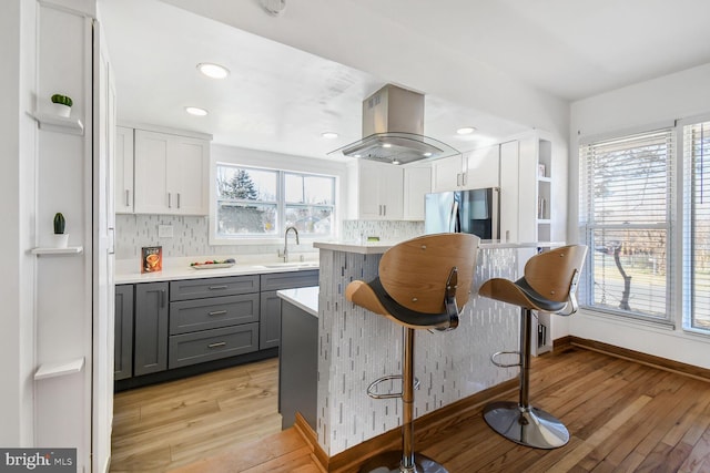 kitchen featuring island range hood, freestanding refrigerator, light countertops, gray cabinets, and a sink