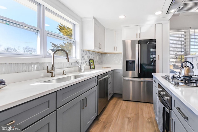 kitchen with light wood-style flooring, stainless steel appliances, a sink, light countertops, and gray cabinets