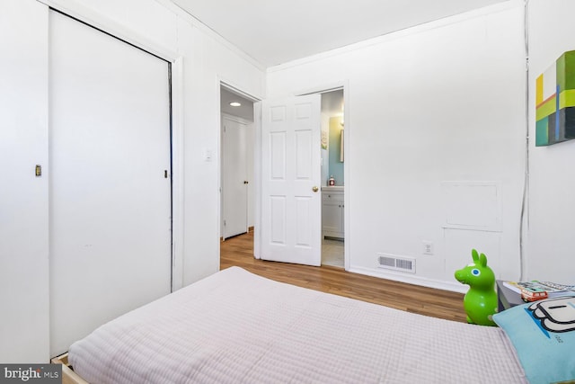 bedroom with connected bathroom, wood finished floors, visible vents, a closet, and crown molding