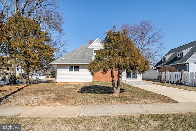 view of front of home with driveway, a chimney, fence, and a front lawn