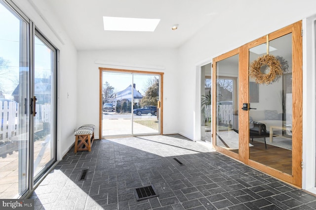 doorway to outside featuring vaulted ceiling with skylight, plenty of natural light, and baseboards