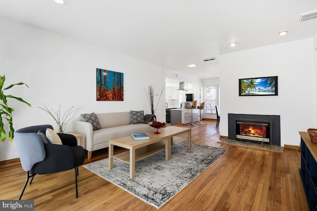 living area featuring a fireplace with flush hearth, visible vents, wood finished floors, and recessed lighting