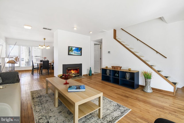 living area with stairs, a notable chandelier, visible vents, a warm lit fireplace, and hardwood / wood-style flooring