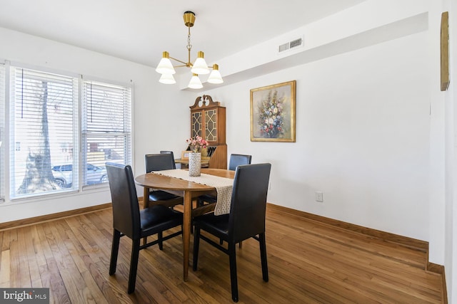 dining room featuring wood-type flooring, visible vents, baseboards, and an inviting chandelier