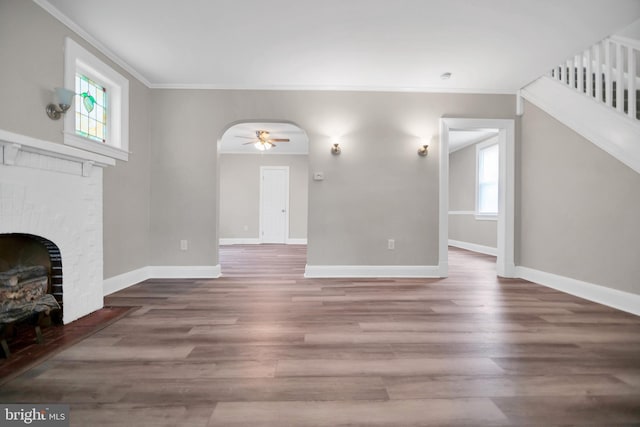 unfurnished living room featuring arched walkways, a brick fireplace, wood finished floors, and a wealth of natural light