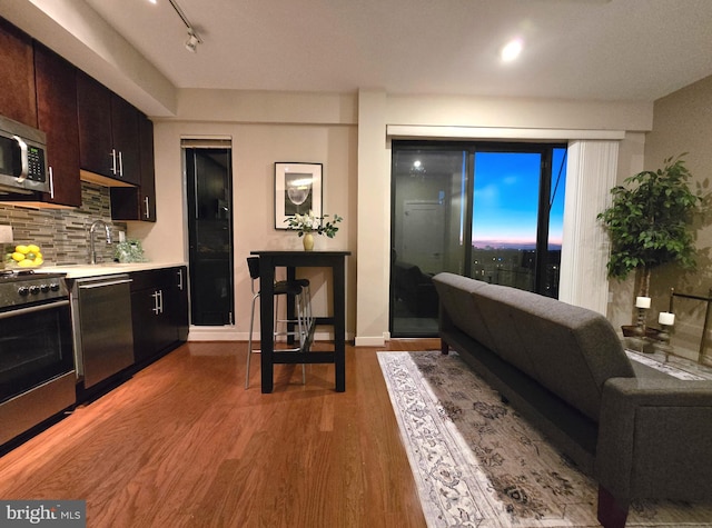 kitchen featuring backsplash, wood finished floors, stainless steel appliances, light countertops, and a sink