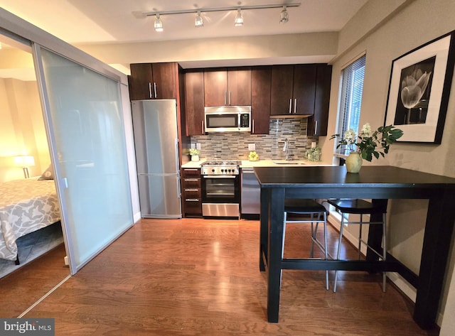 kitchen featuring dark brown cabinetry, tasteful backsplash, appliances with stainless steel finishes, wood finished floors, and a sink