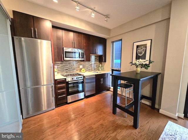 kitchen featuring dark brown cabinetry, light wood-style flooring, a sink, stainless steel appliances, and backsplash