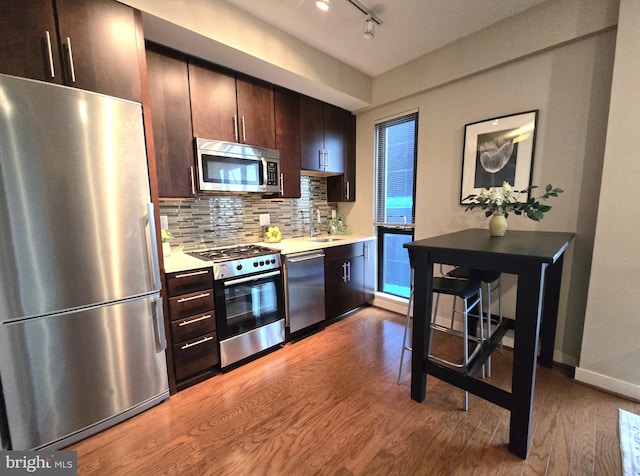 kitchen with dark brown cabinetry, decorative backsplash, appliances with stainless steel finishes, wood finished floors, and light countertops