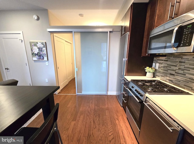 kitchen featuring stainless steel appliances, light countertops, backsplash, dark brown cabinets, and wood finished floors