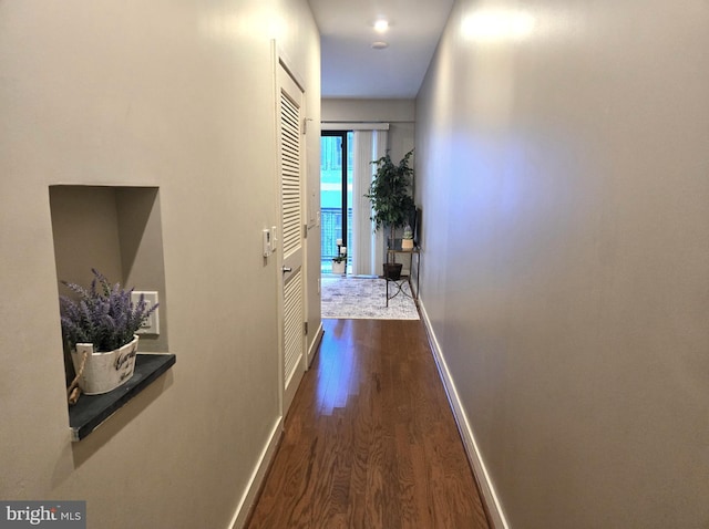 corridor with dark wood-type flooring and baseboards