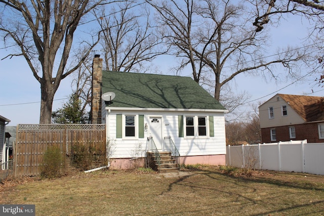 view of front of property with a shingled roof, a front yard, fence, and a chimney