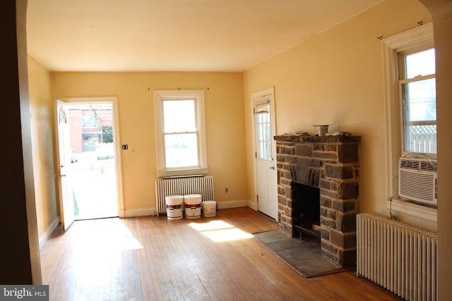 interior space featuring radiator, baseboards, a stone fireplace, and hardwood / wood-style floors