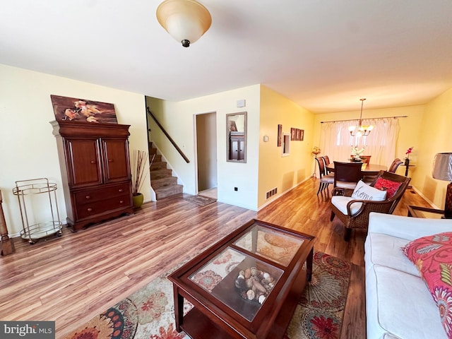 living room with a chandelier, stairway, light wood-type flooring, and visible vents