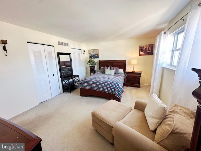 bedroom featuring carpet, two closets, visible vents, and baseboards