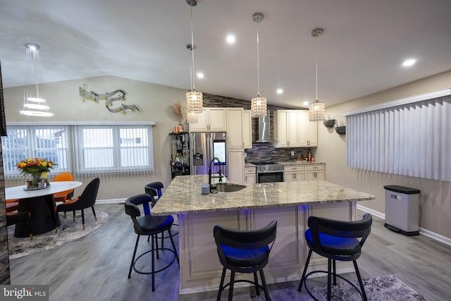 kitchen featuring wood finished floors, stainless steel appliances, wall chimney range hood, and a sink