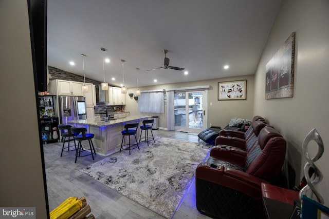 kitchen featuring light stone counters, lofted ceiling, open floor plan, wall chimney range hood, and a kitchen bar