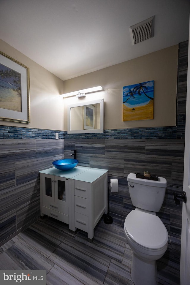 bathroom with tile walls, visible vents, toilet, vanity, and tile patterned floors