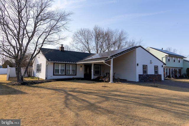 view of front of home featuring a chimney, fence, a front lawn, and solar panels