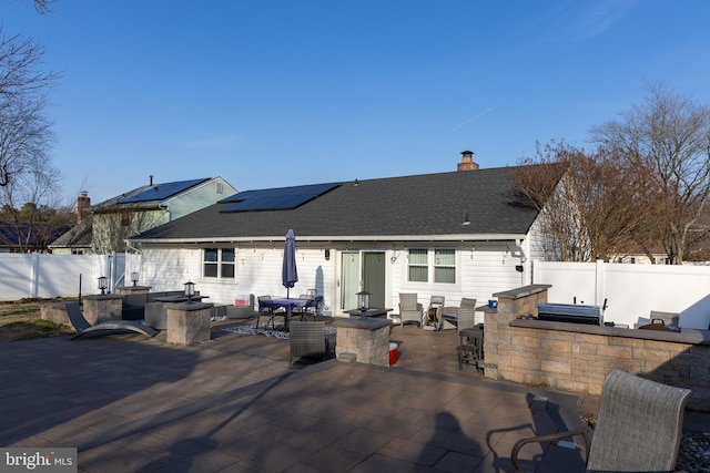 back of house featuring a shingled roof, an outdoor kitchen, solar panels, a fenced backyard, and a patio area