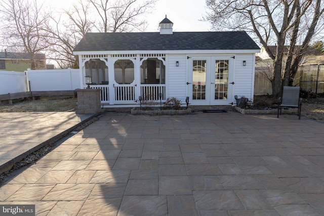 view of front of property featuring a patio area, fence, an outbuilding, and roof with shingles