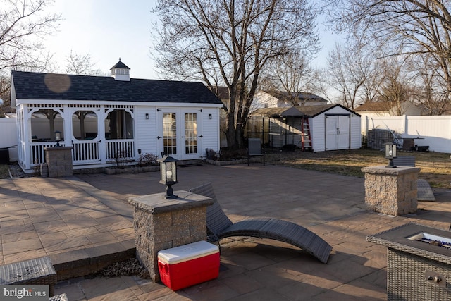 exterior space featuring a shingled roof, an outdoor structure, fence, french doors, and a patio area