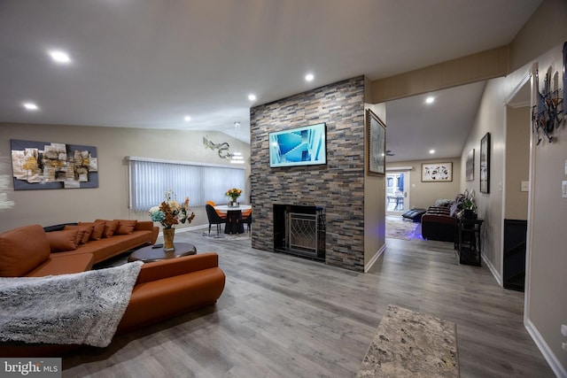 living area featuring lofted ceiling, recessed lighting, a stone fireplace, wood finished floors, and baseboards