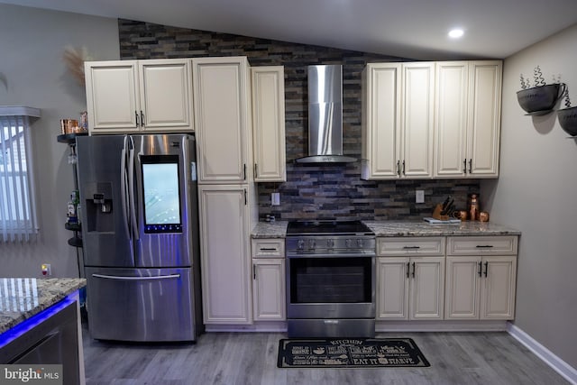 kitchen with light wood-style floors, lofted ceiling, light stone countertops, stainless steel appliances, and wall chimney range hood