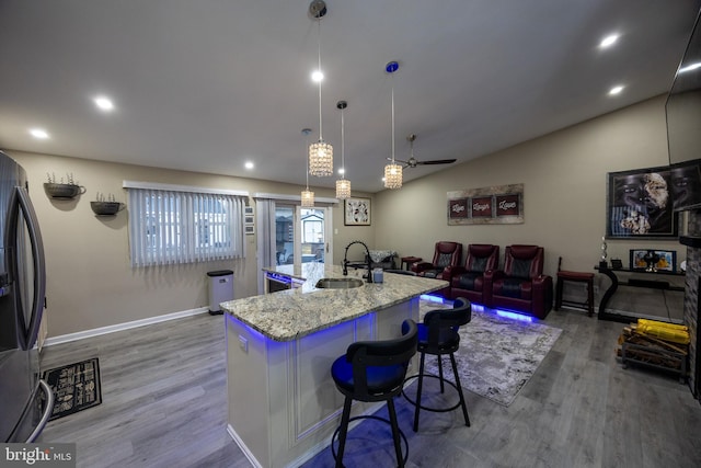 kitchen featuring light stone counters, wood finished floors, a sink, and stainless steel fridge with ice dispenser